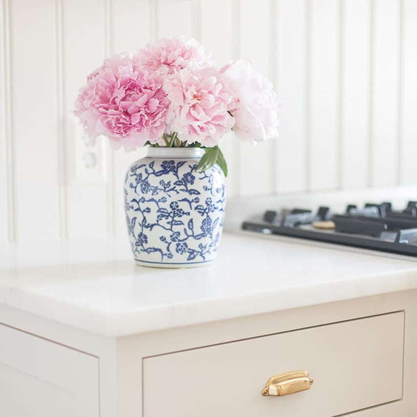 Pink and white peony flowers in a blue vase on a white kitchen counter.