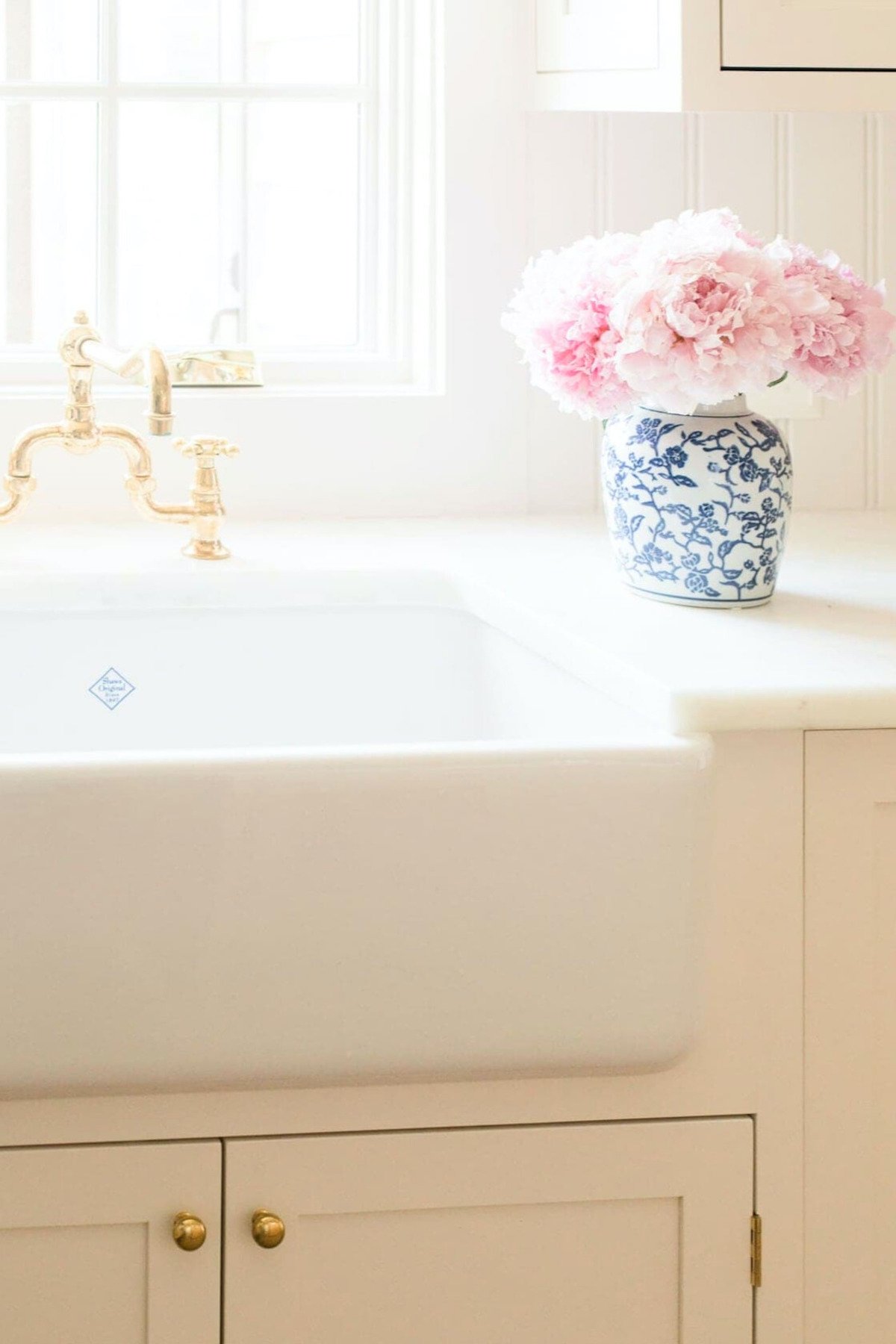 A white kitchen sink with a pink peony in a vase.