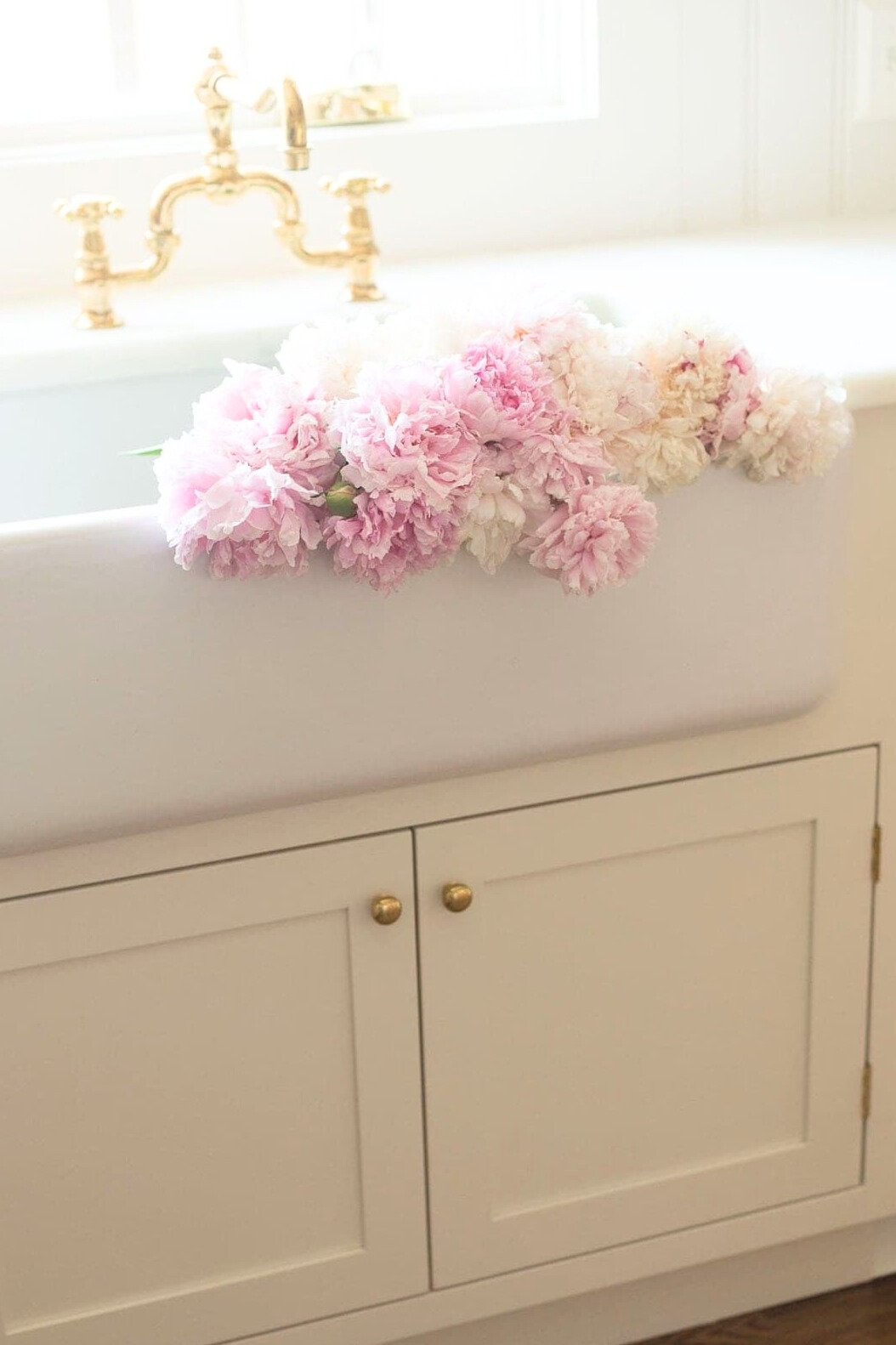 A white kitchen sink with pink peony flowers in it.