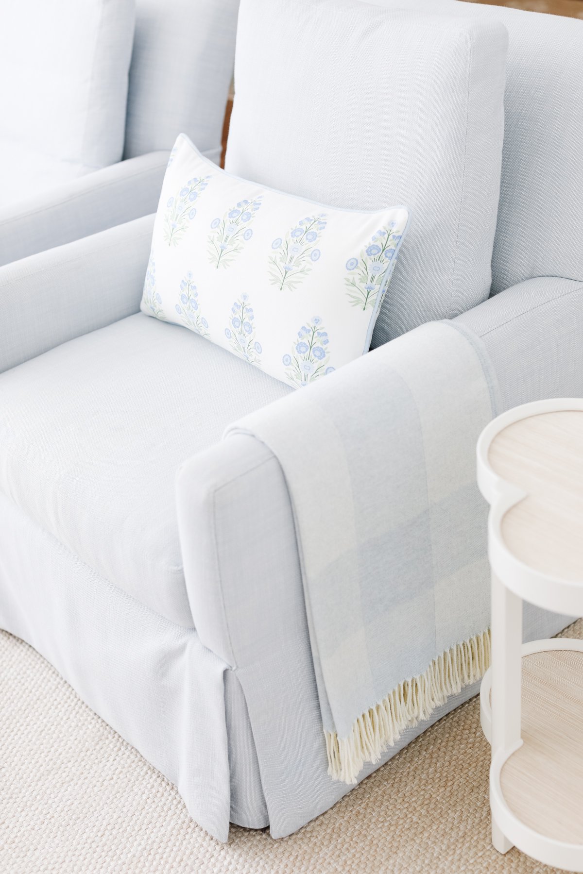 A white chair with a scalloped pillow and a blanket.