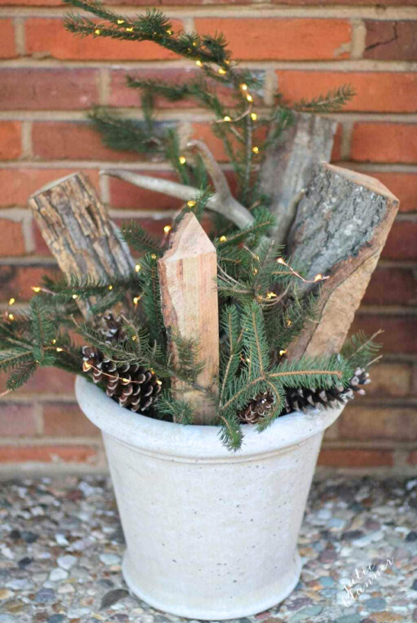 A winter porch planter full of firewood, evergreens, antlers and twinkling lights.