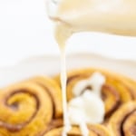Pouring cream cheese icing on cinnamon rolls.