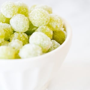 Bowl of boozy sugared green grapes on a white background.