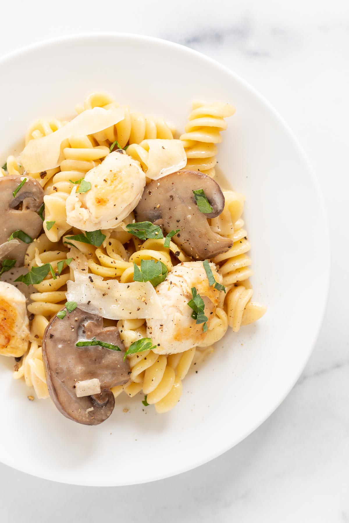 A plate of chicken mushroom pasta with scallops and chopped herbs, served on a white background.