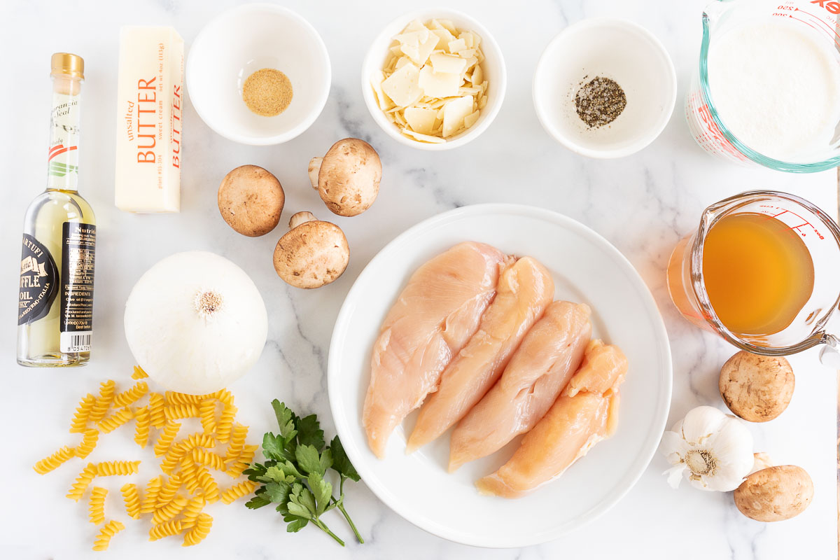 Overhead view of ingredients for a chicken mushroom pasta recipe, arranged on a marble surface, 