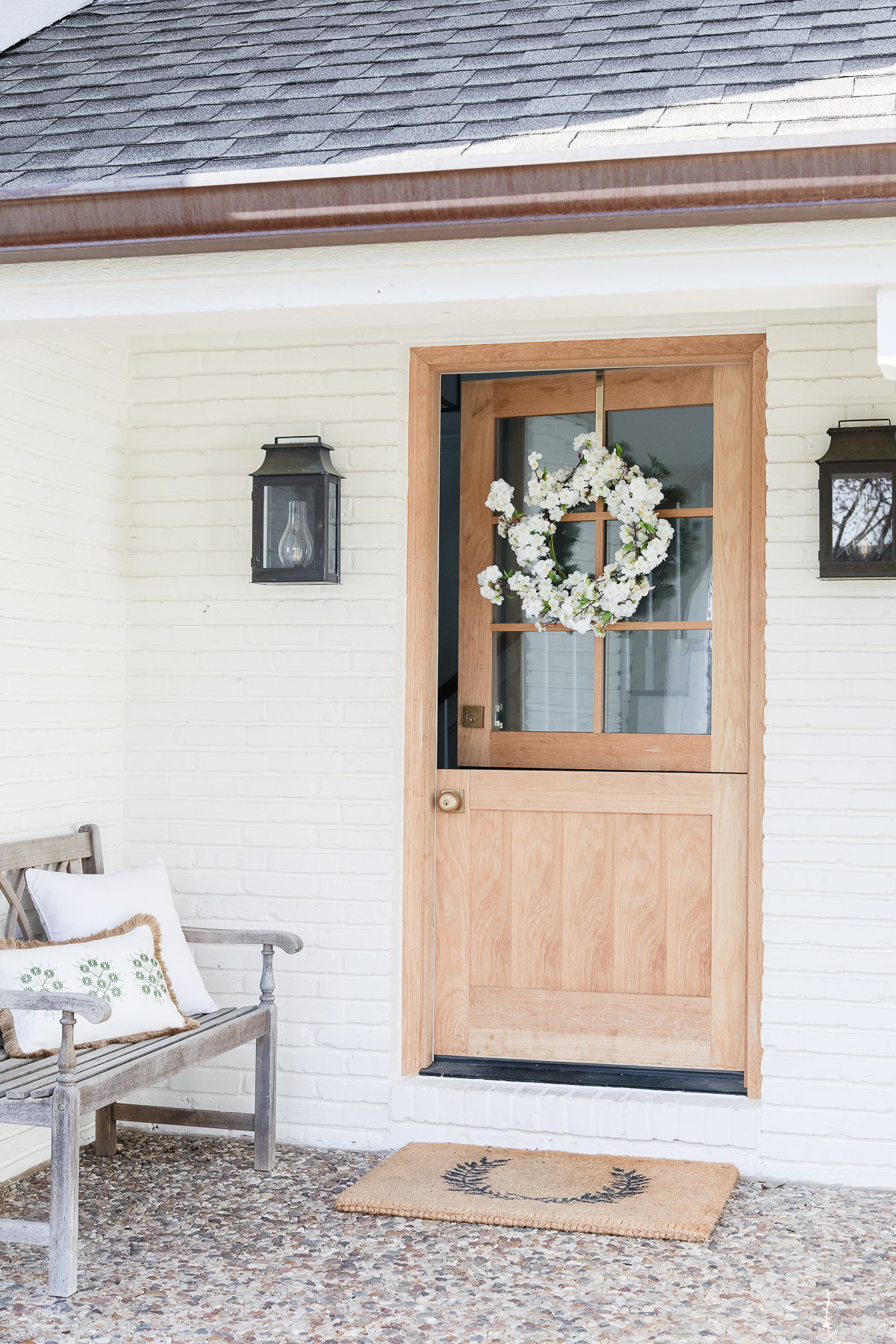 A white brick home with a wooden dutch door and copper gutters. 