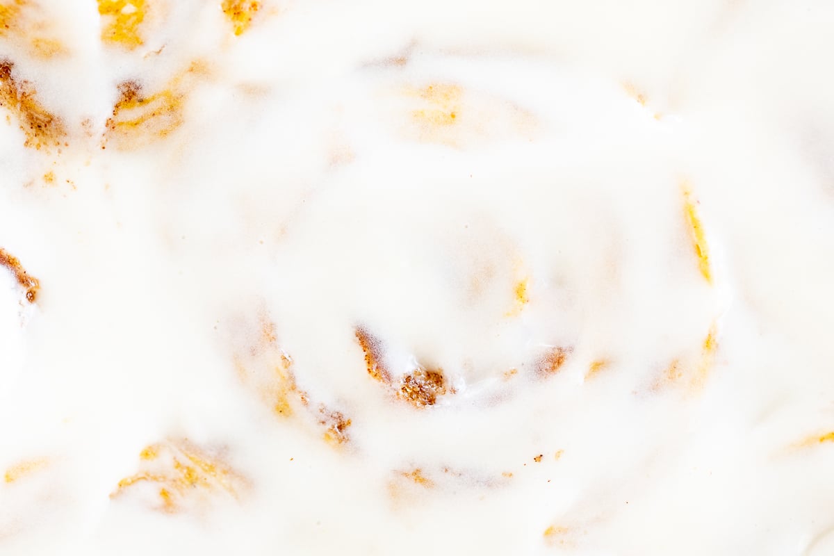 Close-up of a cream cheese icing for cinnamon rolls, poured on top of a plate of rolls