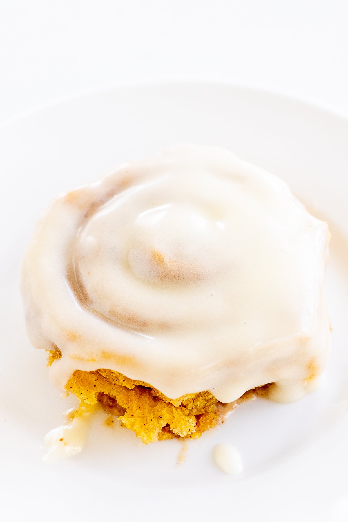 A cinnamon roll with cream cheese icing on a white plate, partially bitten.
