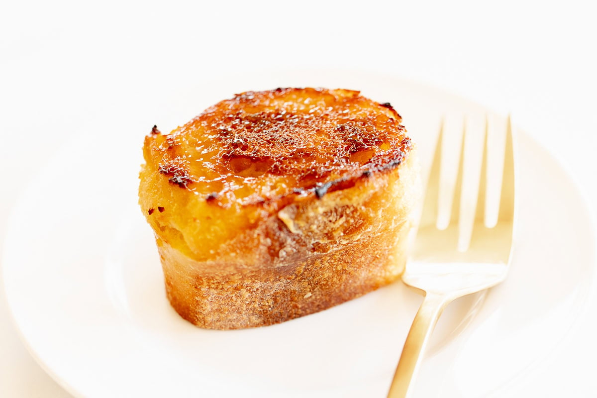 Creme Brulee French toast slice on a white plate with a gold fork.
