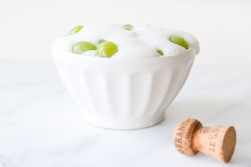Bowl of yogurt and boozy grapes with a champagne cork on the side.