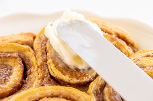 Spreading cream cheese icing on a freshly baked cinnamon roll.