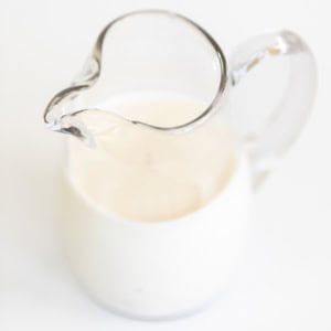 A glass pitcher filled with creamy milk on a white background, with focus on the spout.