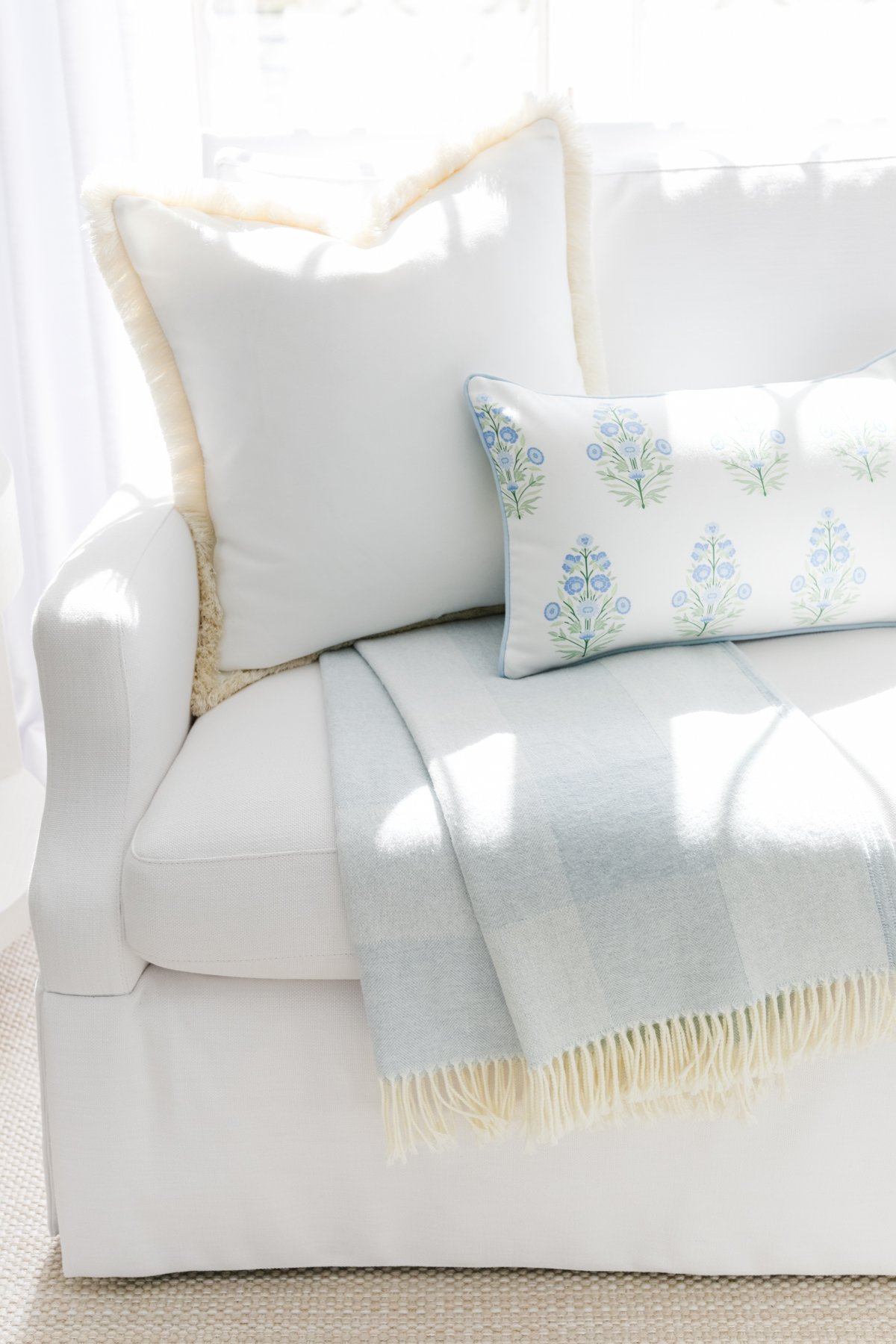 A white sofa with two decorative pillows and a blue and white fringed blanket draped over the armrest.