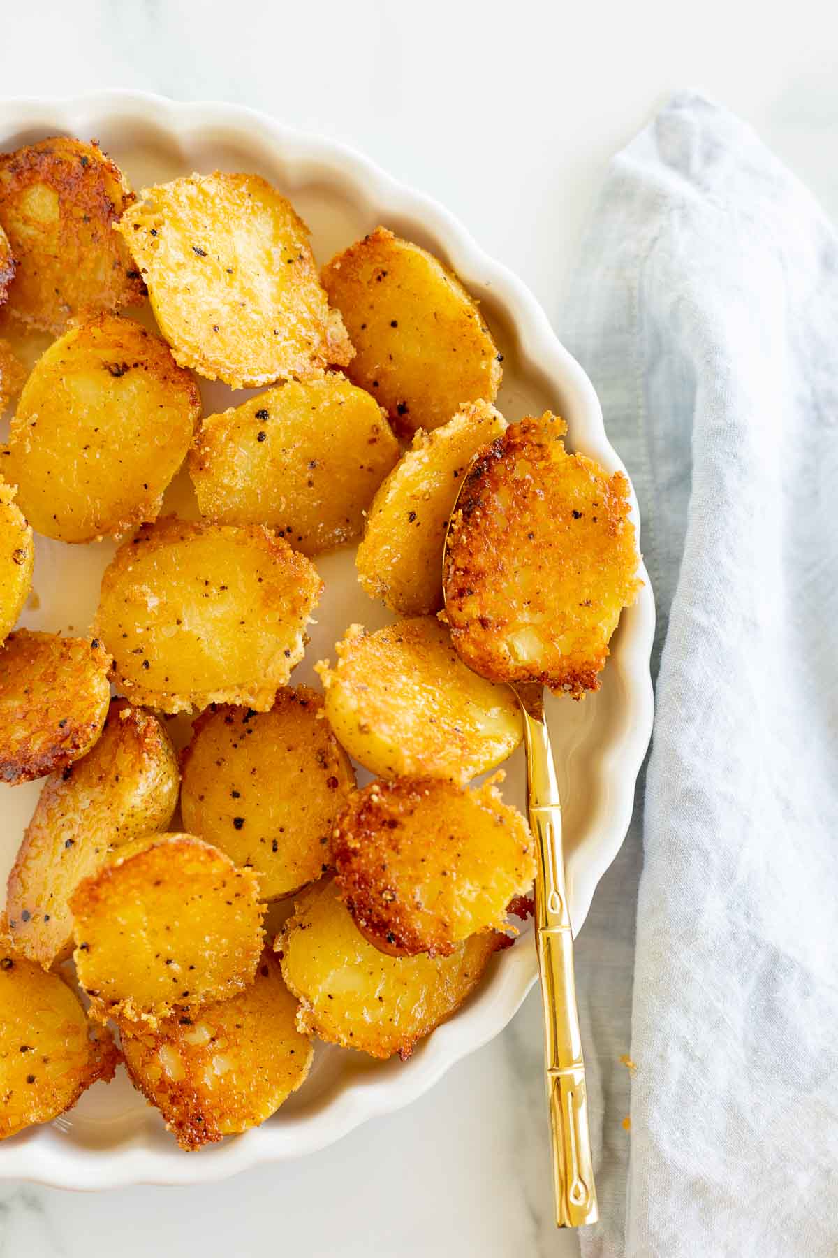 Parmesan crusted potatoes in a white dish on a white countertop. 