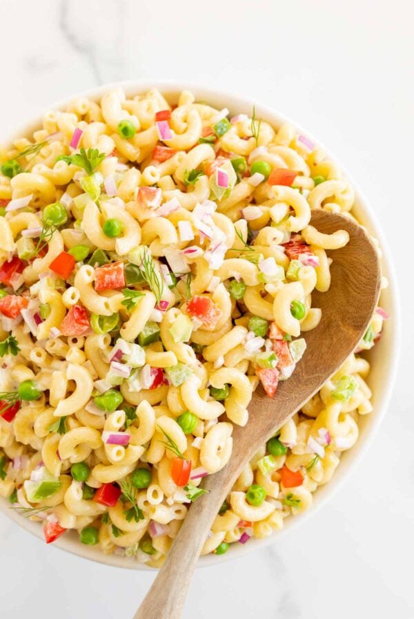 A white bowl full of macaroni salad, with a wooden spoon inside.