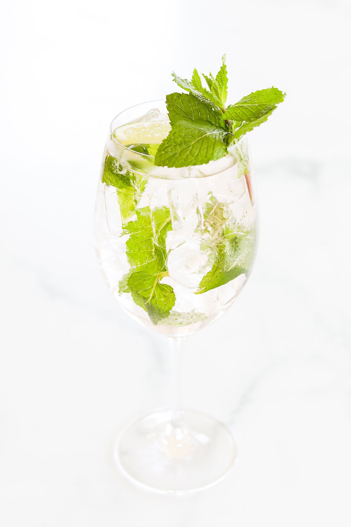 A glass of iced rosé spritz with lime slices and fresh mint leaves on a white background.
