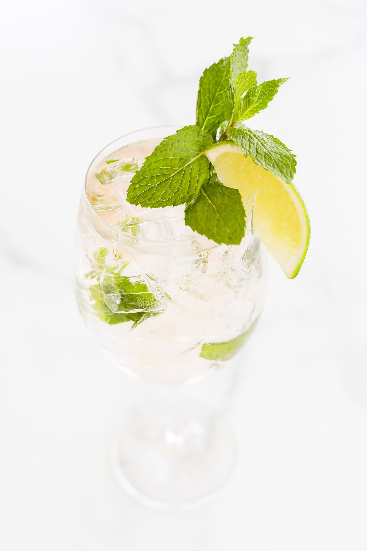 A glass of iced rosé spritz with lime slices and fresh mint leaves on a white background.