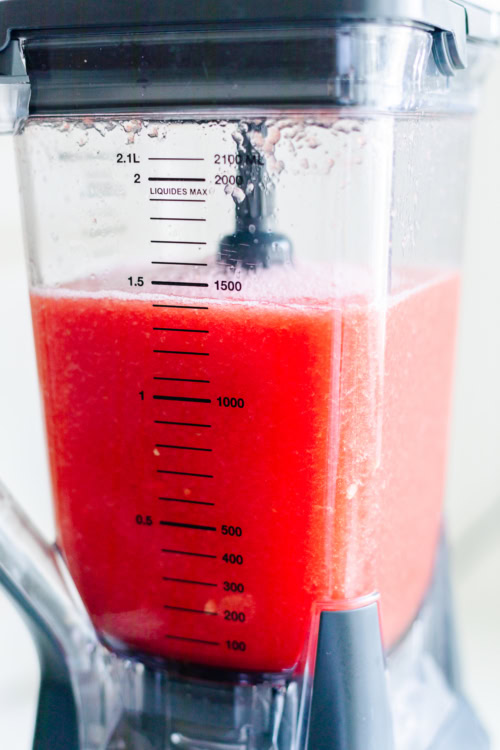 Close-up of a blender jar filled with watermelon juice, marked with measurement lines up to 2.1 liters. The liquid appears to be blended to a smooth consistency.