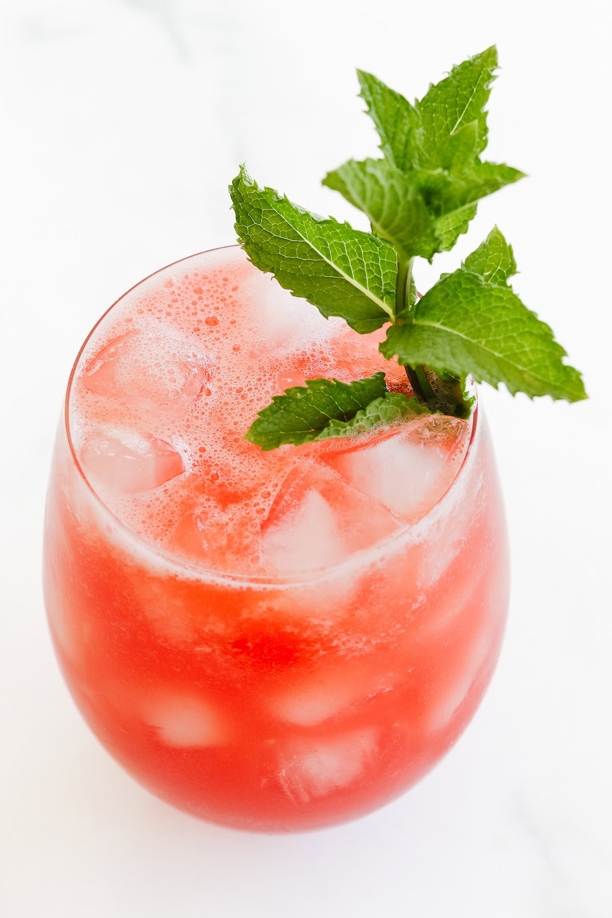 A glass of iced watermelon juice with foam on top, garnished with a sprig of fresh mint.