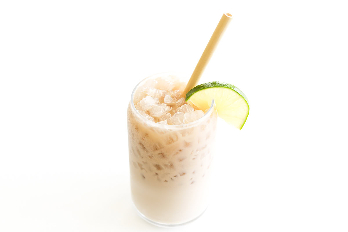 A glass of iced Dirty Dr Pepper with a lime slice on the rim and a straw, filled with crushed ice, against a plain white background.