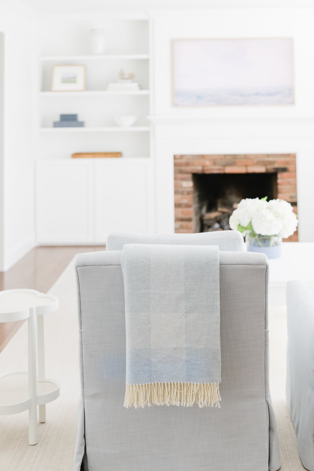 A cozy living room showcases a gray armchair with a light blanket draped over it, a prime spot for relaxation. A brick fireplace, white shelves, and a small side table complete this inviting space.