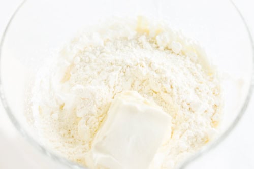 Close-up of a mixing bowl with white flour and a lump of softened butter, coming together like the first steps in creating Gooey Butter Cake Ice Cream perfection.