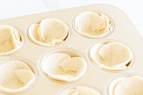 Close-up of a muffin tin with unbaked dough pressed into each cup, resembling small tart shells, perfect for making delicious Mexican Breakfast Cups.