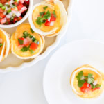 Mexican Breakfast Cups: Small tortilla egg cups filled with eggs, topped with chopped tomatoes, jalapenos, and cilantro, served on a white plate with a side of salsa.