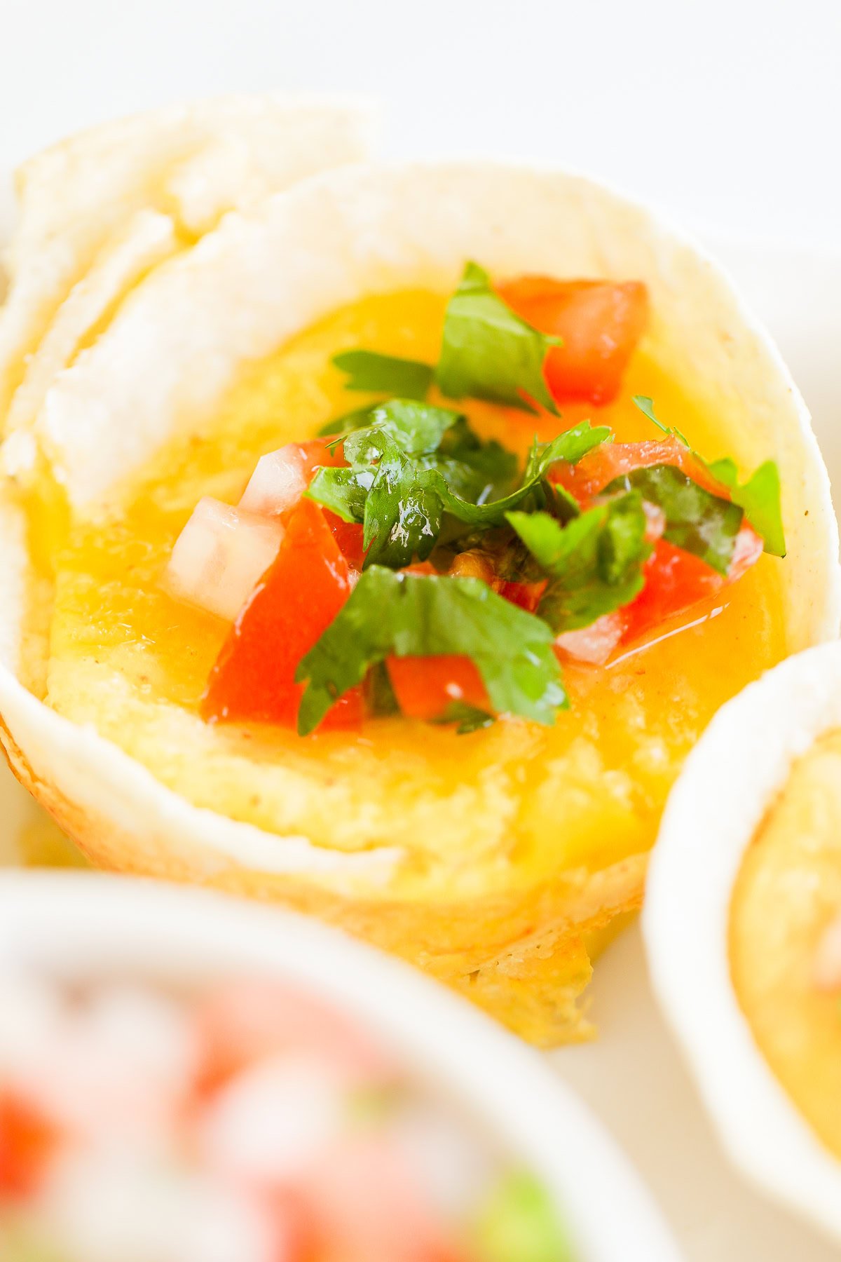 A close-up of a Mexican Breakfast Cup filled with scrambled eggs, topped with diced tomatoes and cilantro.