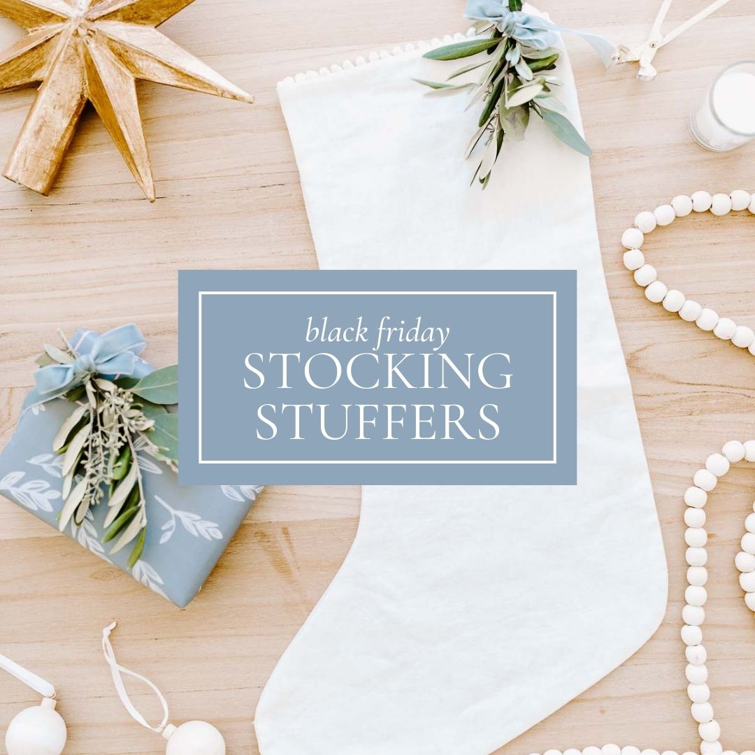 White stocking with greenery sits on a wooden surface. A wrapped gift and white bead garland are nearby, ready for the holidays. Text reads 