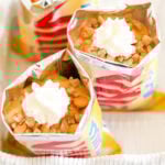 Opened bags of chips filled with pudding, butterscotch chips, and crushed nuts, topped with whipped cream—a delightful twist on butterscotch pie in a bag.