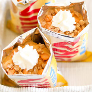 Opened bags of chips filled with pudding, butterscotch chips, and crushed nuts, topped with whipped cream—a delightful twist on butterscotch pie in a bag.