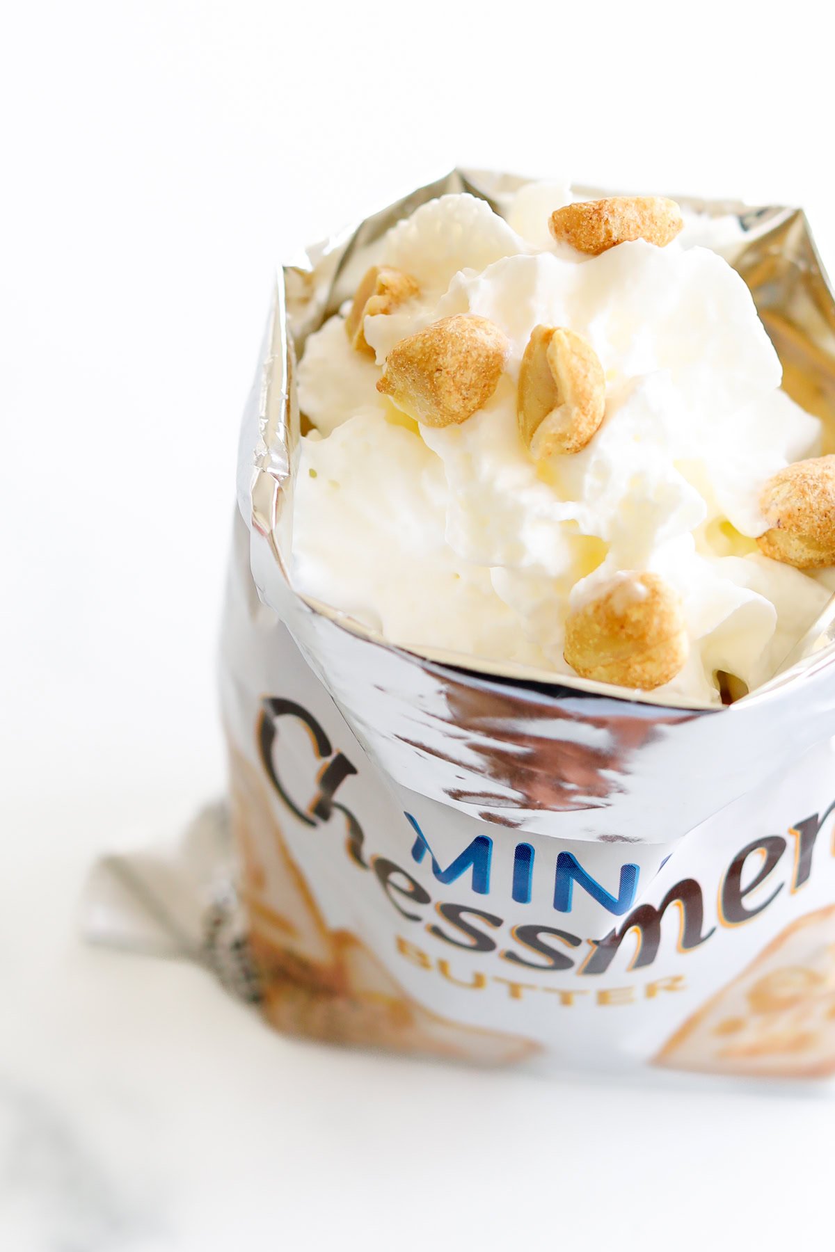 Open snack bag filled with whipped cream and topped with peanuts.