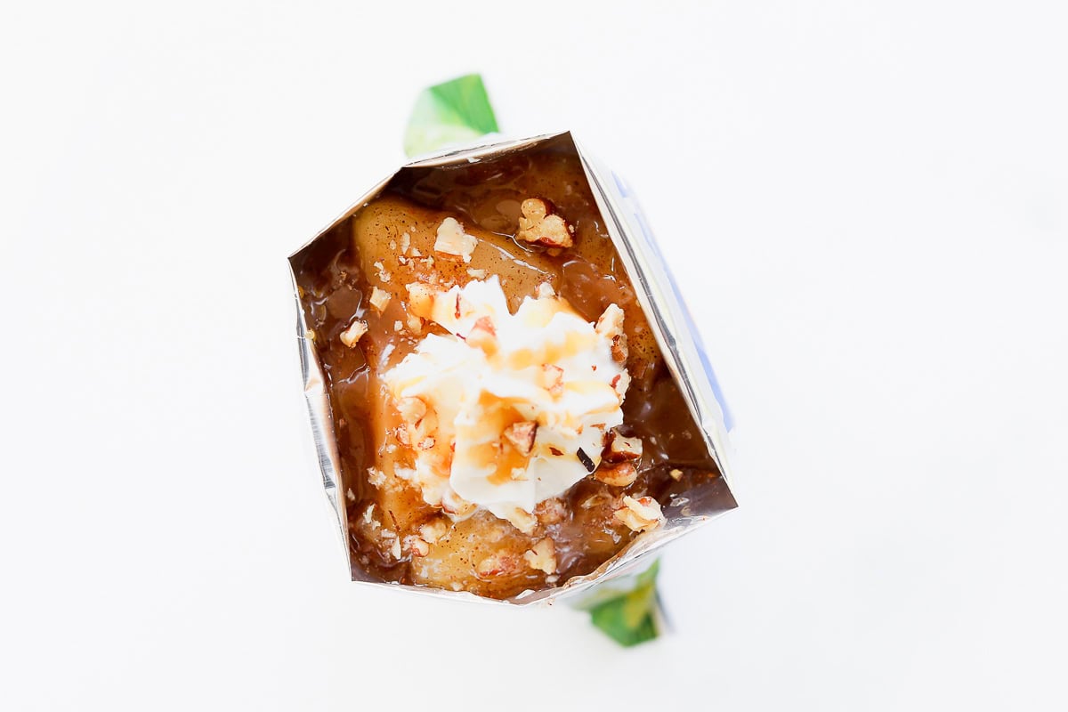 An open apple pie in a bag topped with whipped cream and nuts.