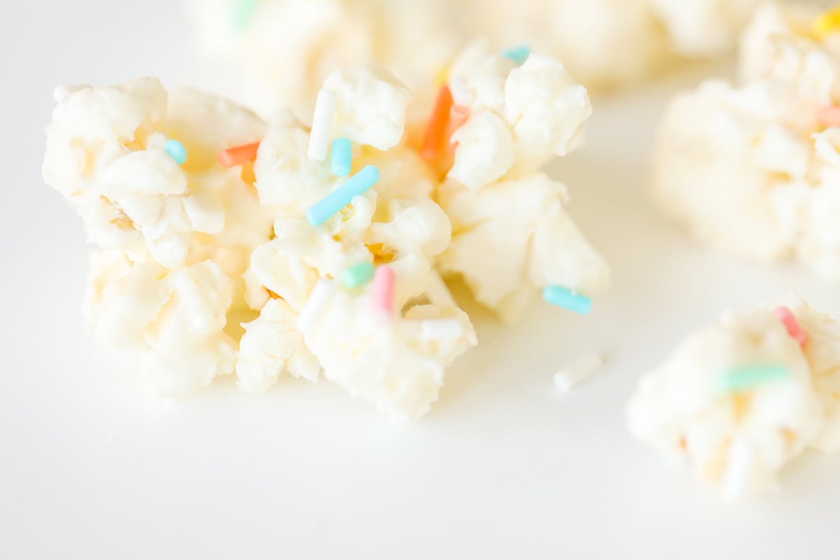 Close-up of Birthday Cake Popcorn clusters adorned with colorful sprinkles on a white background.