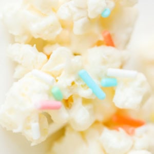 A close-up of Birthday Cake Popcorn reveals a delightful treat, with each piece covered in white frosting and adorned with colorful sprinkles.