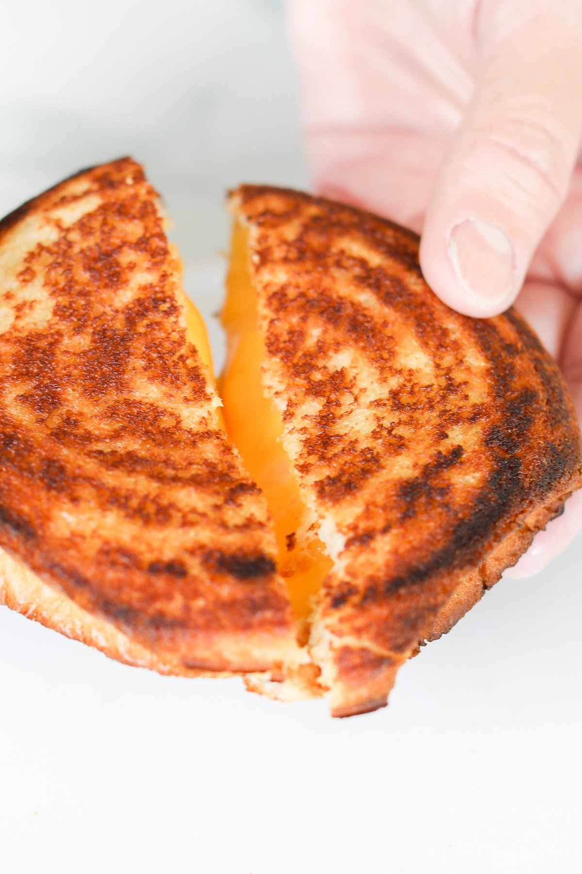 A hand holding a campfire grilled cheese sandwich, pulled apart to reveal gooey melted cheese that brings the cozy warmth of a fireside treat.