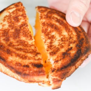 A hand holding a campfire grilled cheese sandwich pulled apart, revealing the gooey, melted cheese inside.