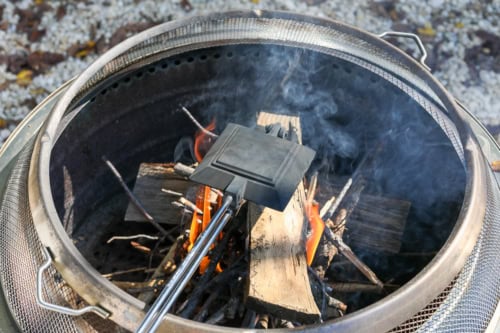 A pie iron sizzles as it turns a simple sandwich into a delicious campfire grilled cheese, nestled among the crackling firewood and twigs.