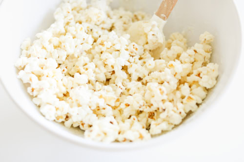 A bowl of Birthday Cake Popcorn with a wooden spoon, viewed from above, against a white background.