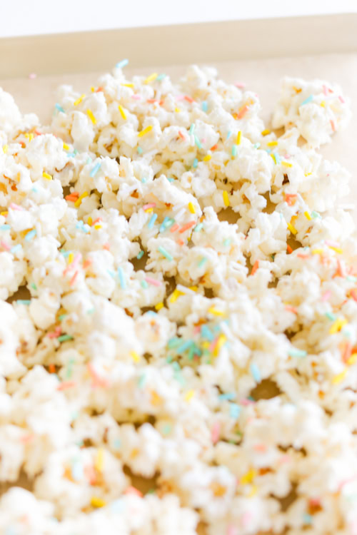 Birthday Cake Popcorn: White-coated popcorn with colorful sprinkles spread out on a baking sheet, resembling a festive celebration.