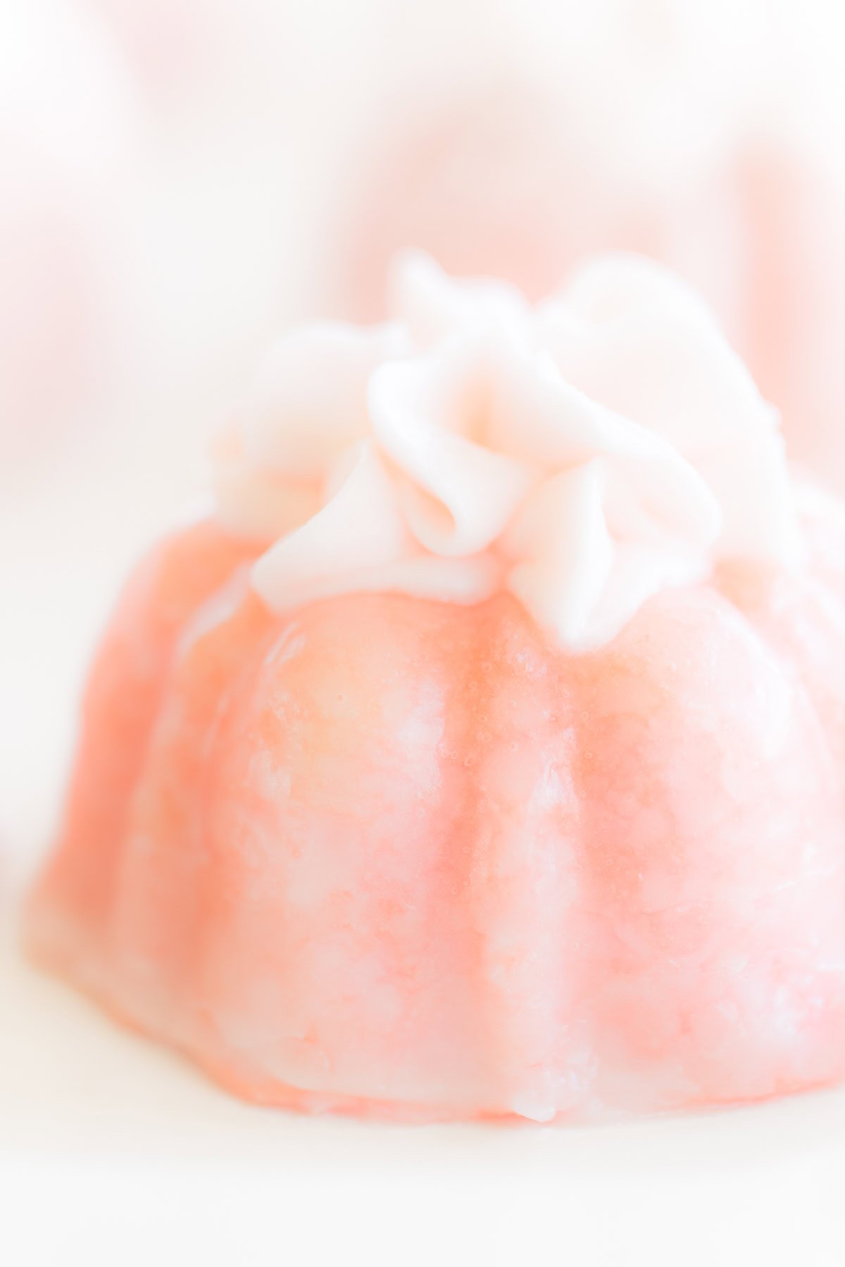 A close-up of a pink jelly dessert topped with luscious white champagne frosting, set against a light background.