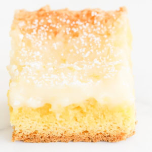 Close-up of a slice of lemon gooey butter cake with a golden crust, creamy top layer, and sprinkled with powdered sugar.