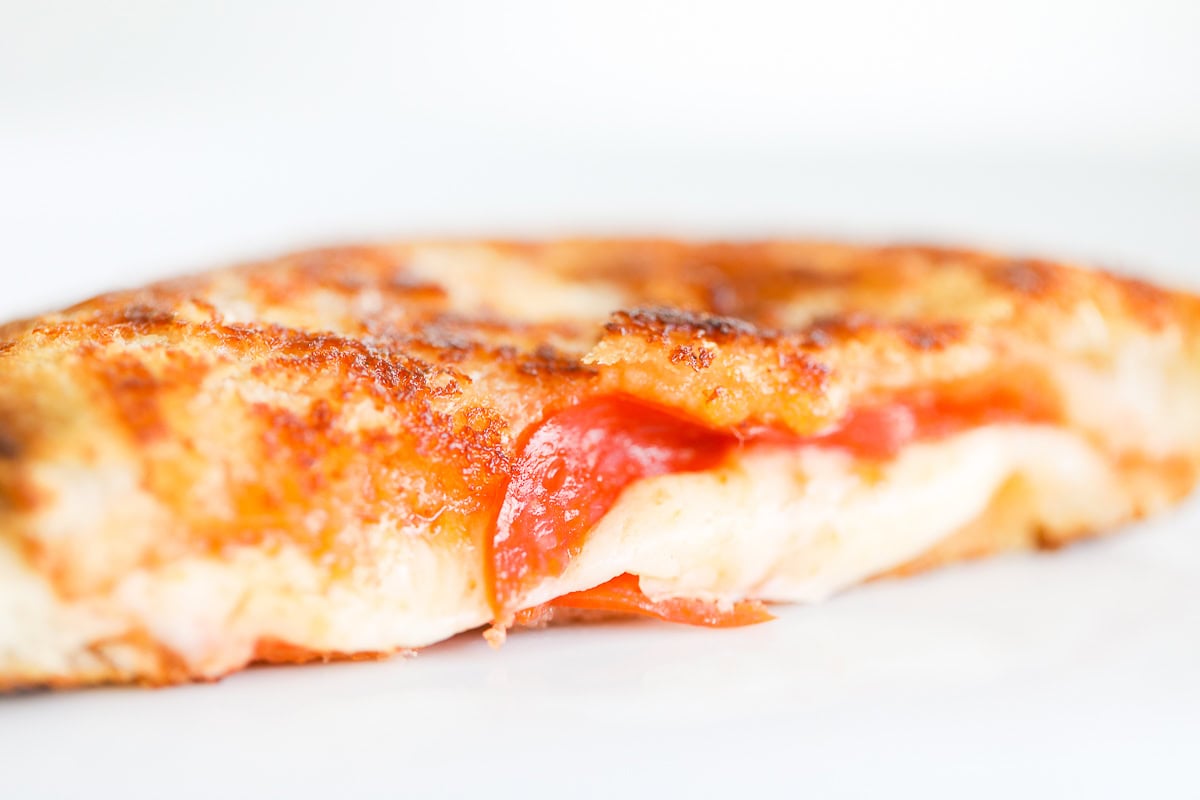 Close-up of a slice of Campfire Pizza with melted cheese, pepperoni, and a crispy crust on a white background.