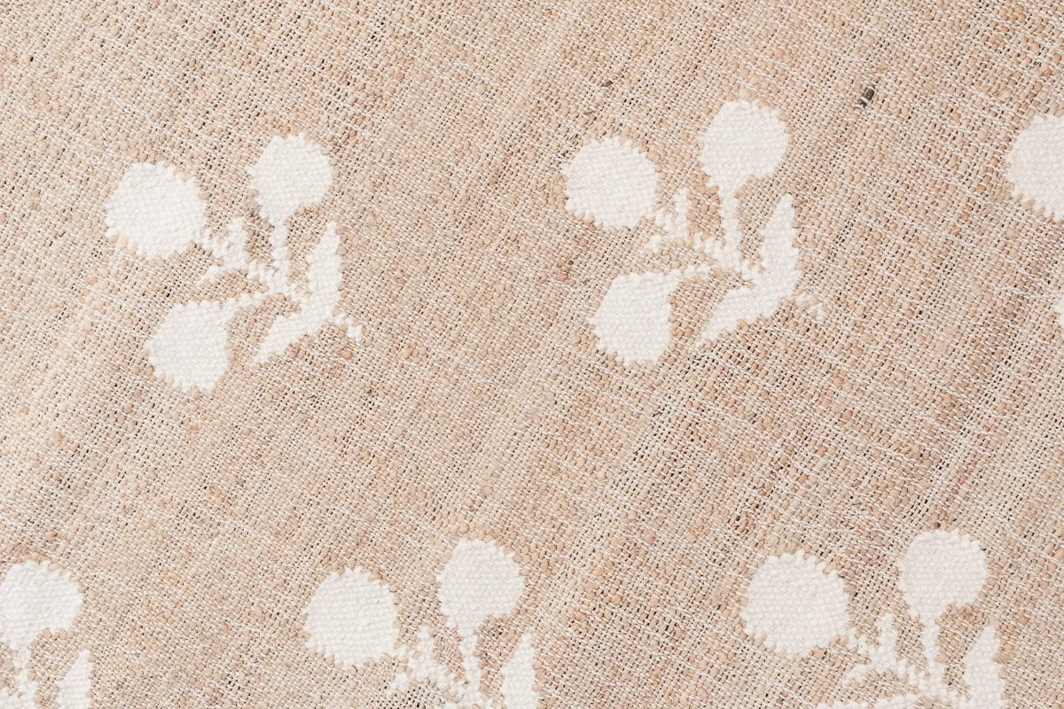 Beige textured fabric with a woven pattern and white floral motifs arranged in a repeating design, perfect for achieving the pottery barn look for less.