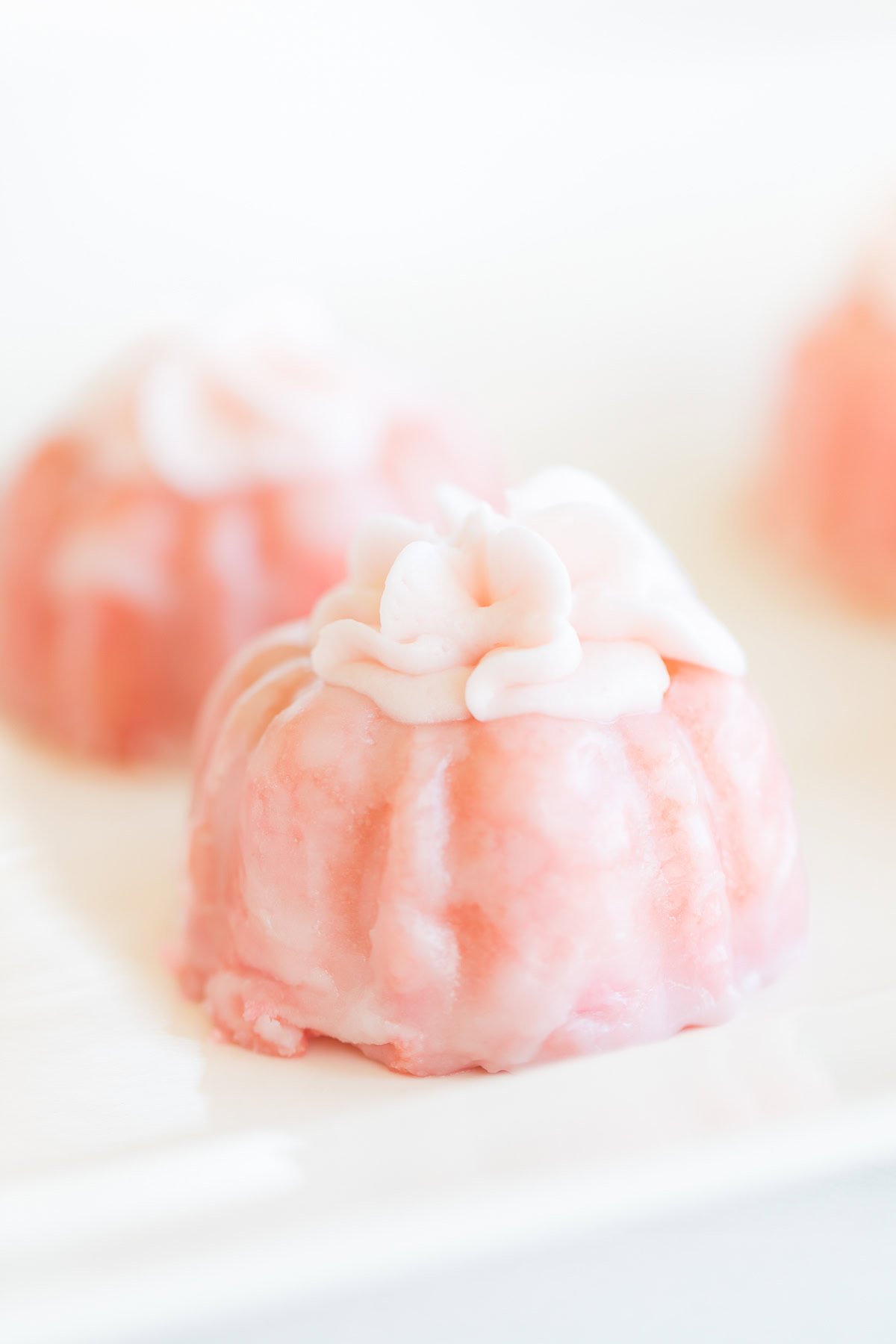 Close-up of a pink frosted mini cake with champagne frosting and decorative icing on top, resting elegantly on a white plate.