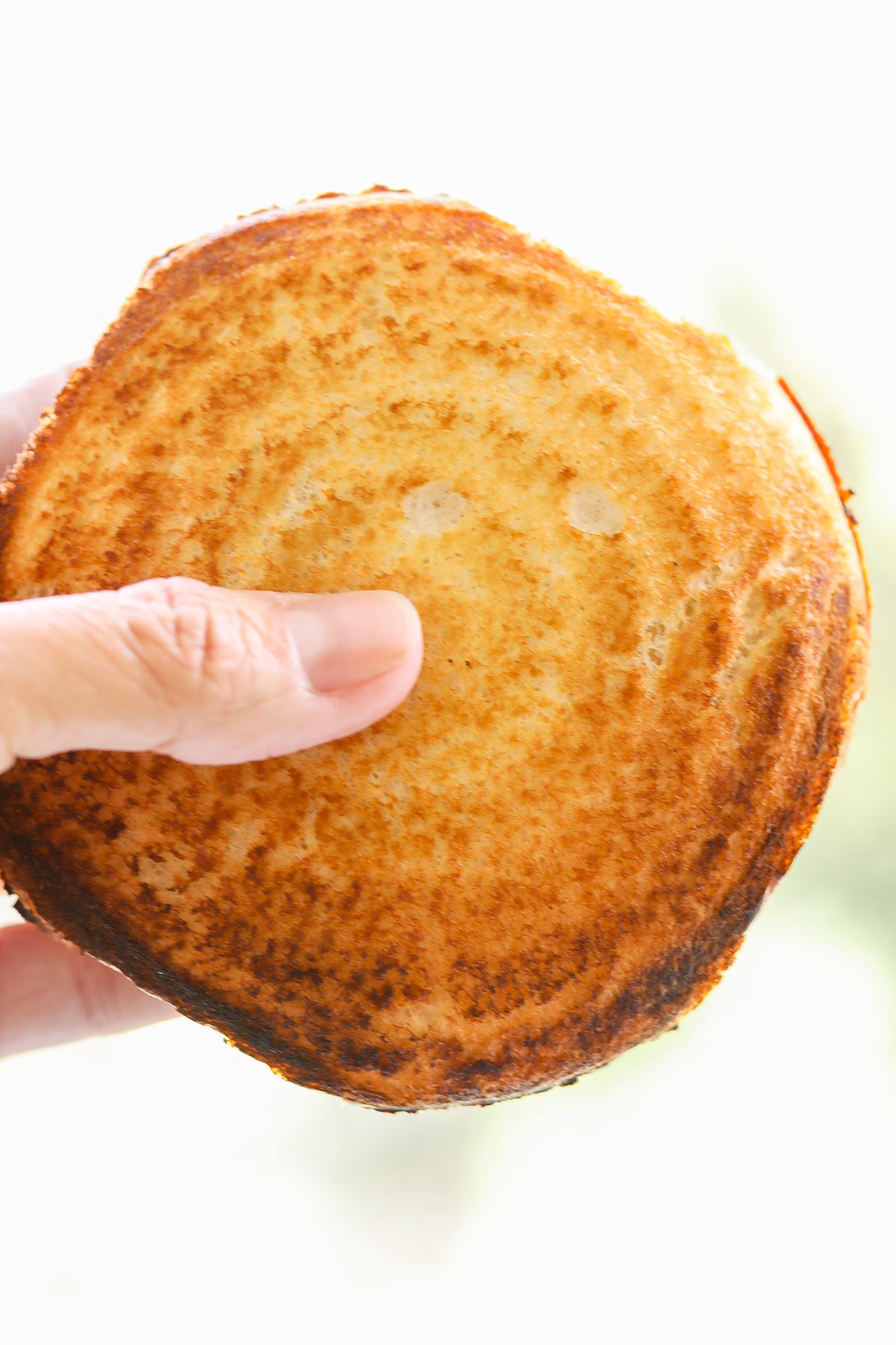 Hand holding a perfectly toasted, round Pudgy pie with golden-brown crust against a blurred background.