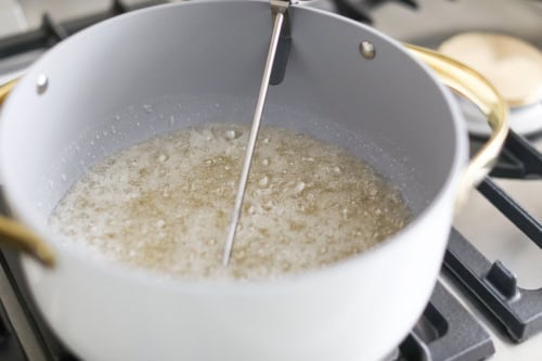 A pot of liquid simmering on the stovetop with a thermometer immersed, as the peanut brittle mixture bubbles away inside.