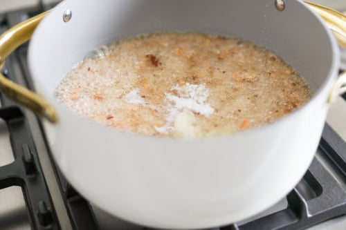 A pot on the stove contains a bubbling mixture with visible chunks and foam, resembling the early stages of making peanut brittle, likely indicating cooking or frying.