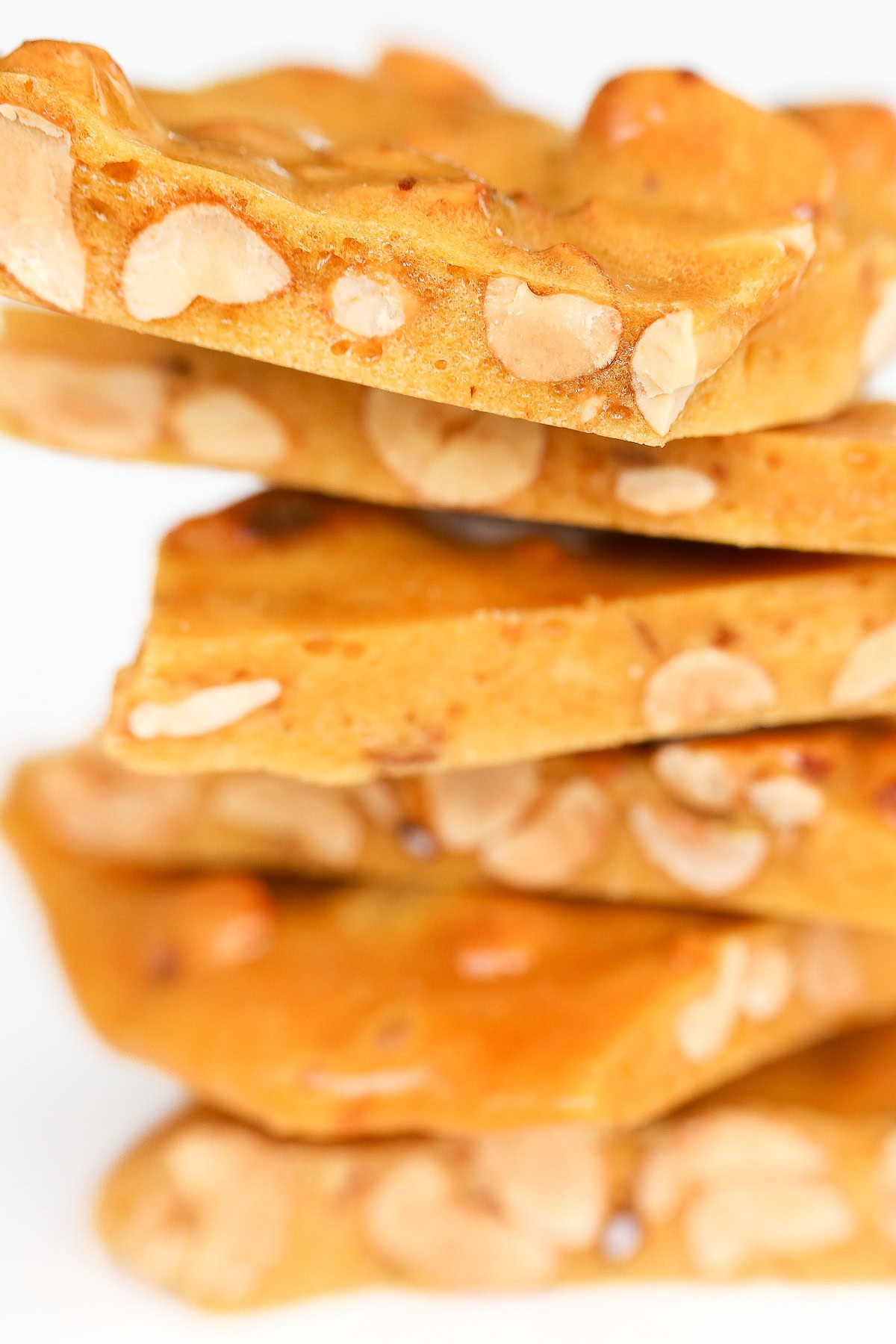 A delightful stack of peanut brittle pieces showcases visible peanuts embedded in a golden-brown caramelized sugar base.